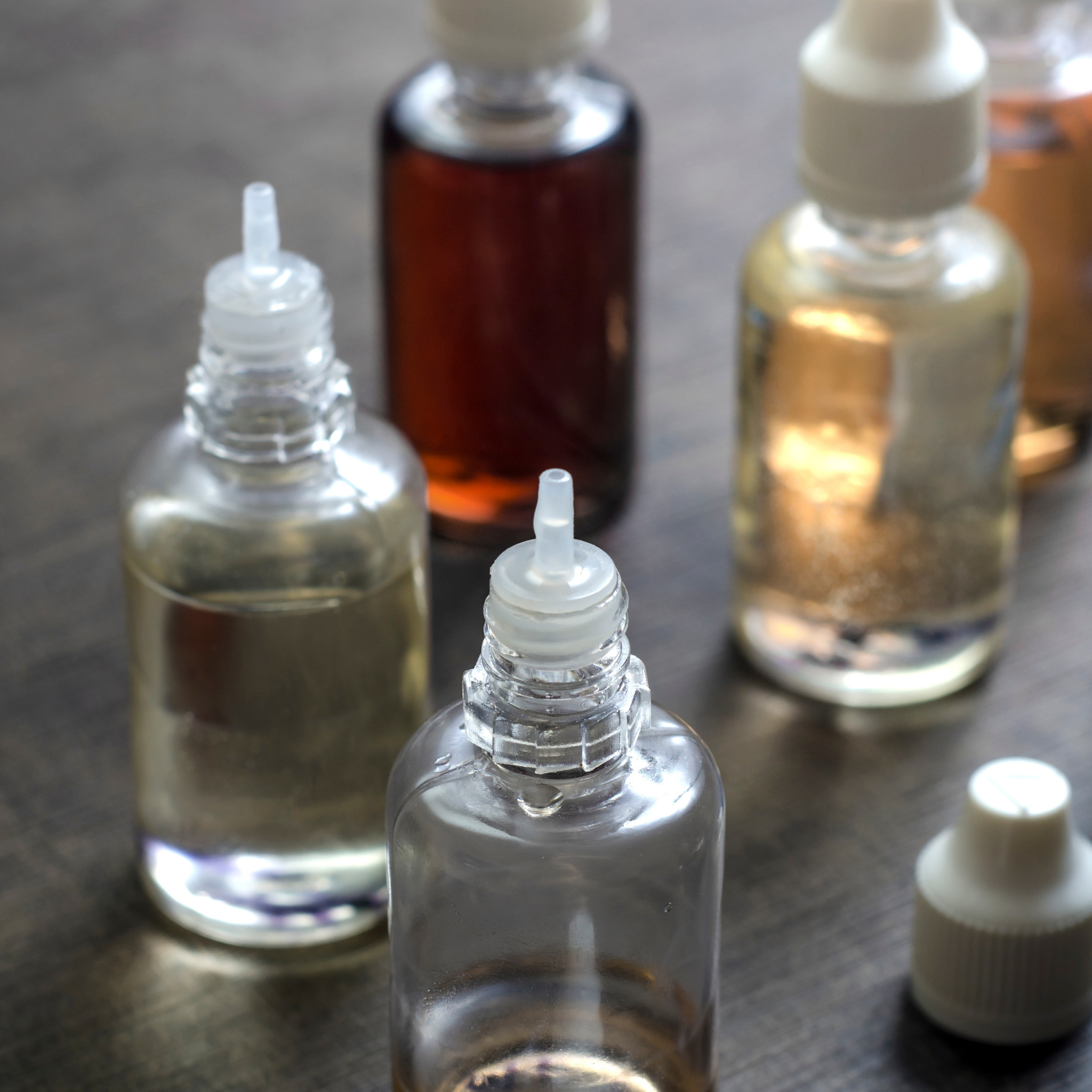 Flacon neutre de concentré DIY pour e‑liquides, entouré d’un halo blanc chaud sur fond sombre, avec accessoires de préparation (pipette, flacons et bécher)